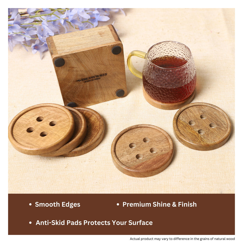 Delightful button-shaped wooden coasters made from natural mango wood, shown with a matching holder, textured glass mug, and gold spoon on a light fabric surface